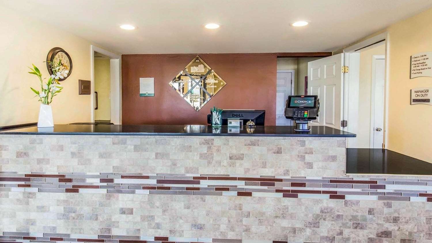 Image of a modern reception desk area with a decorative vase, clock, wall mirror, and computer.