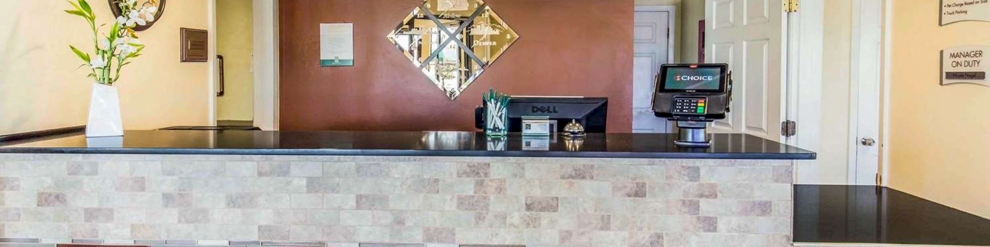 Image of a modern reception desk area with a decorative vase, clock, wall mirror, and computer.