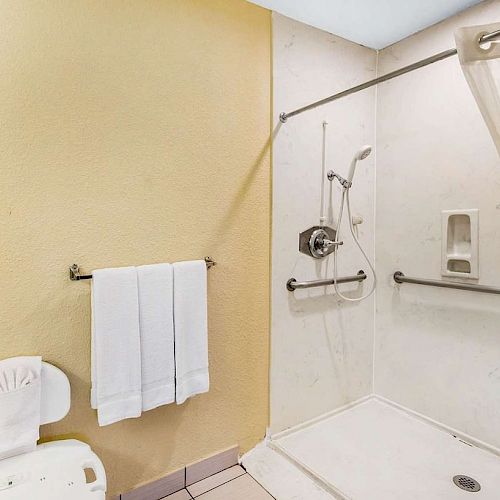 An accessible bathroom features a shower with grab bars, a shower chair, and towel racks, with neatly hung white towels.