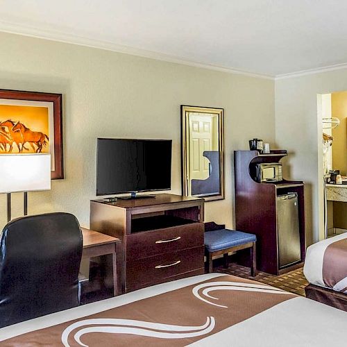 The image shows a hotel room with two double beds, a desk and chair, a TV, a mini-fridge, a microwave, and a framed picture on the wall.