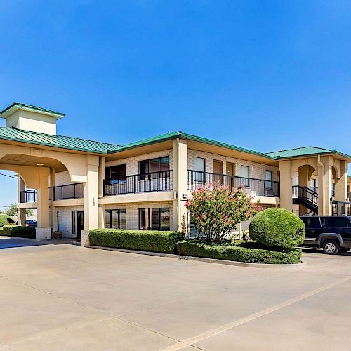 This image shows a two-story building that appears to be a hotel or motel, with a parking lot in front and a car parked.