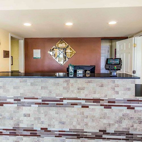 A reception area with a modern tile counter, a computer, wall clock, decorative mirror, plant, and informational signs.