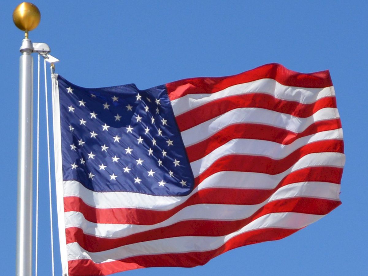 The image features the flag of the United States, with its distinctive red and white stripes and white stars on a blue field, waving on a flagpole.