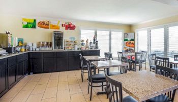 This image shows a brightly lit breakfast area with multiple tables and chairs, a counter with snacks, drinks, and a coffee machine.