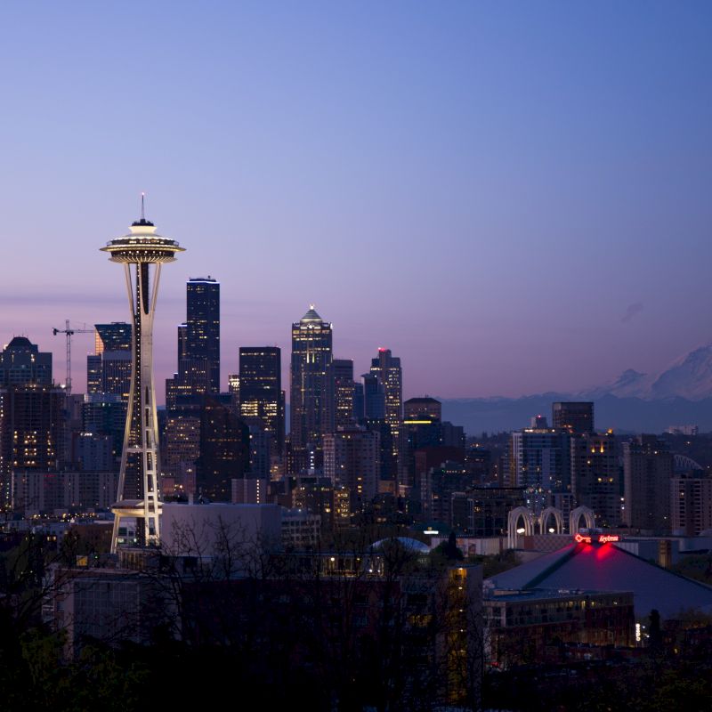 This image shows the Seattle skyline at dusk, featuring the iconic Space Needle, downtown buildings, and Mount Rainier in the background.