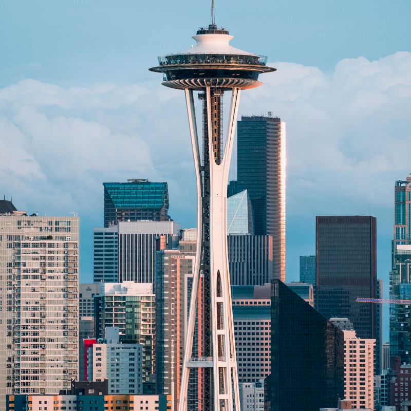 The image shows the Seattle skyline with the prominent Space Needle tower in the foreground, surrounded by various modern skyscrapers and buildings.