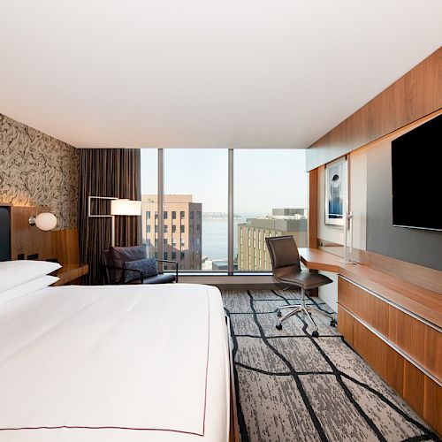 This image shows a modern hotel room with a large bed, TV, desk, chair, and city view through the window.