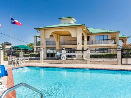 The image shows an outdoor swimming pool with a building in the background and flags on the left side.